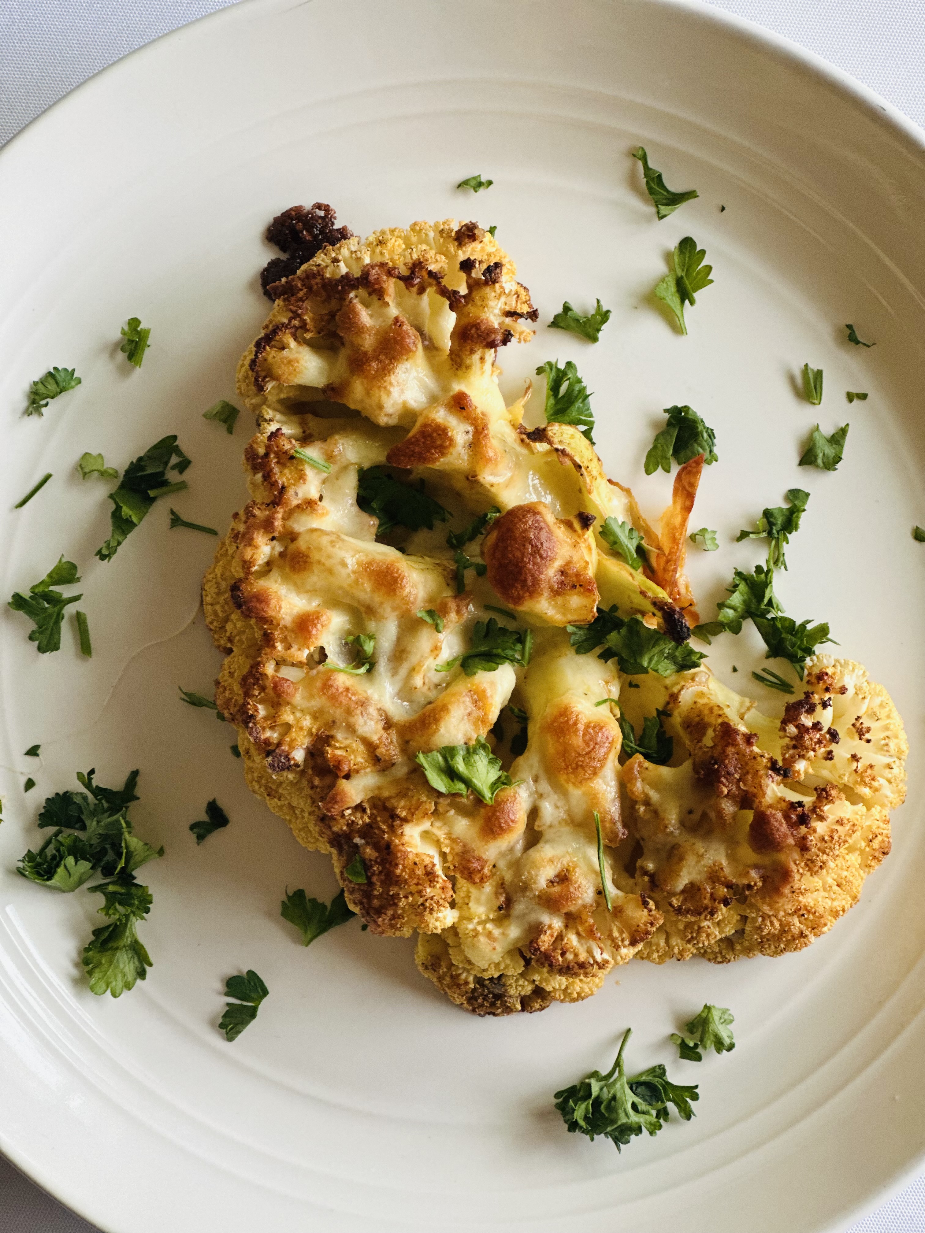 A photo of a delicious cauliflower steak topped with cheese and fresh parsley