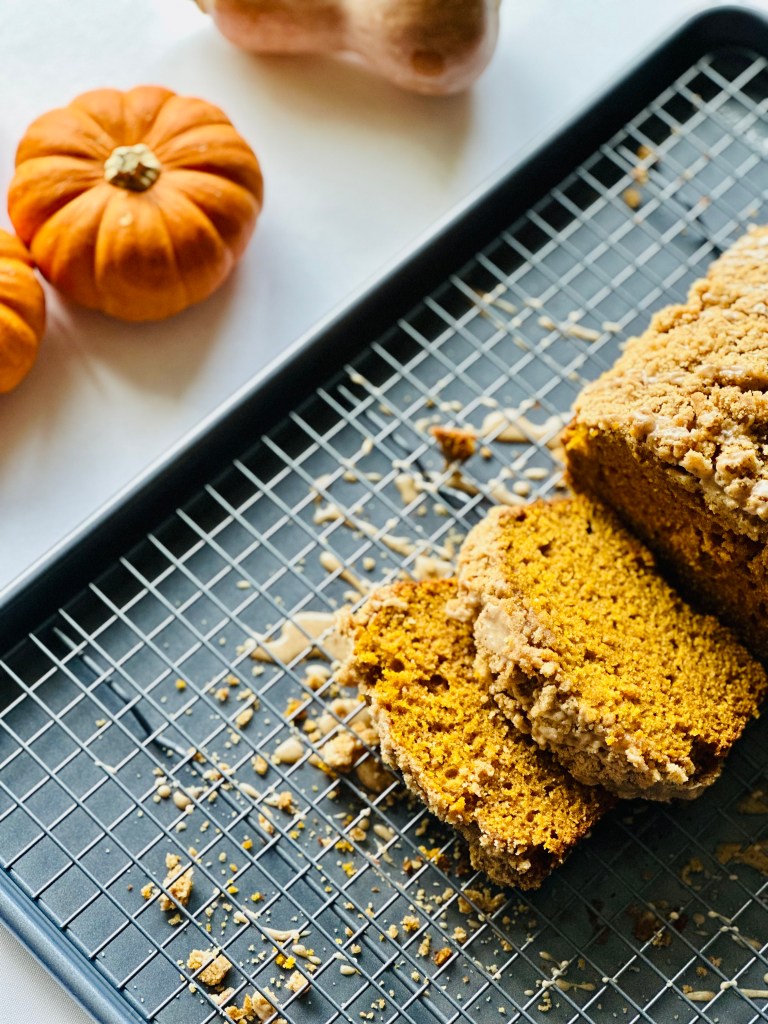 A loaf of pumpkin spice crumb cake on a wire rack topped with pumpkin-spice glaze