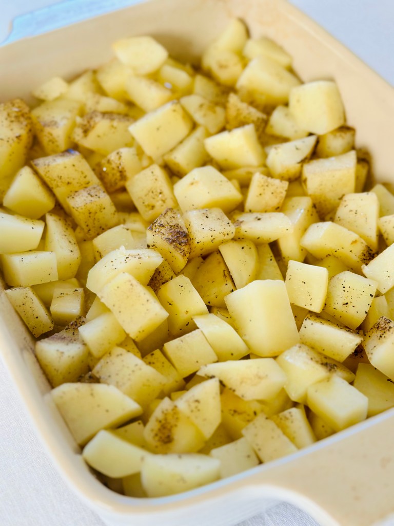 A baking dish full of diced potatoes, seasoned with olive oil, salt, and pepper