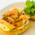 A bagel sandwich with cream cheese, cucumber, smoked salmon, capers, and arugula