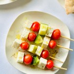 A plate with four skewers threaded with cherry tomatoes, cubes of feta, and cucumber
