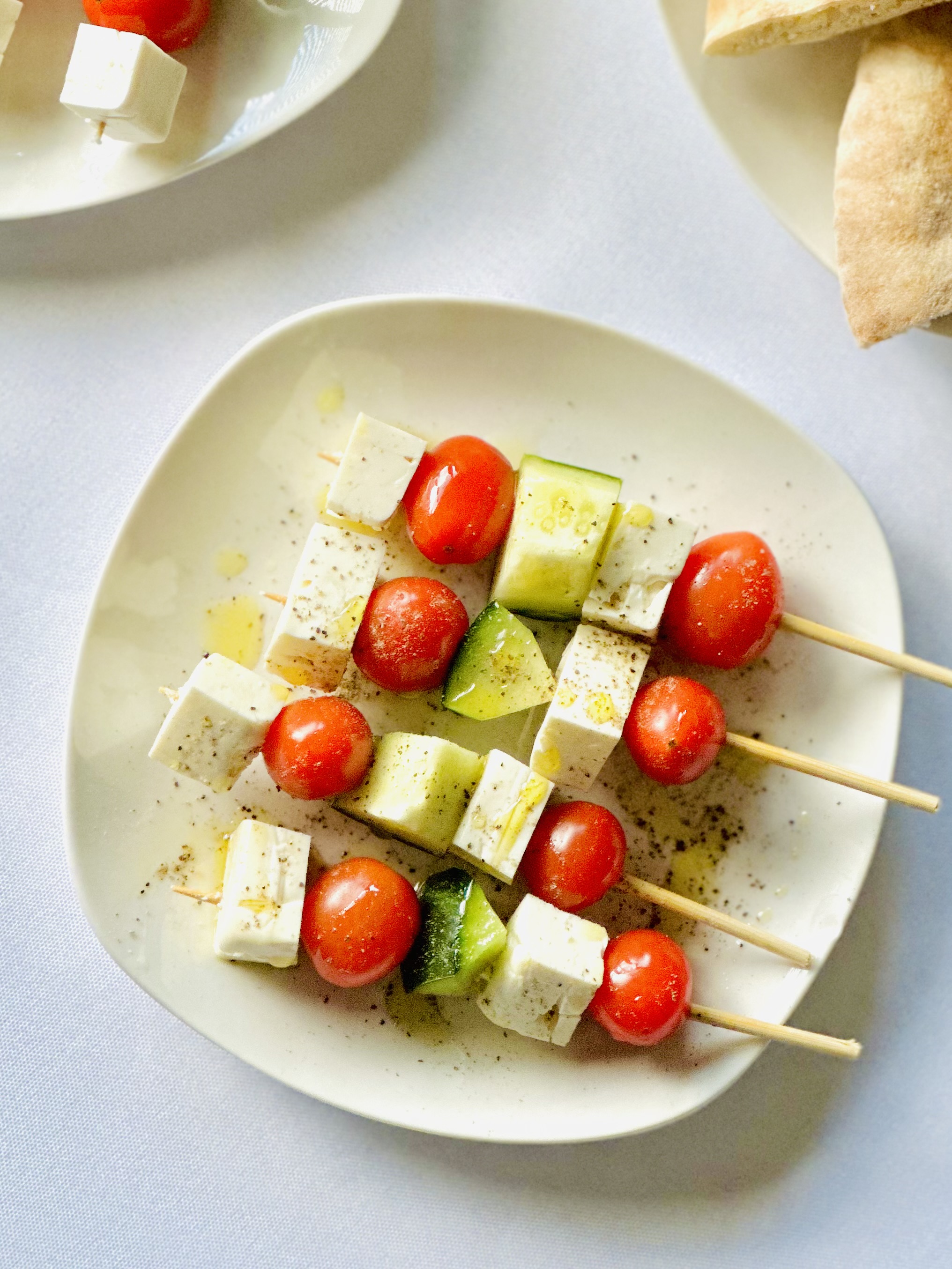 A plate with four skewers threaded with cherry tomatoes, cubes of feta, and cucumber
