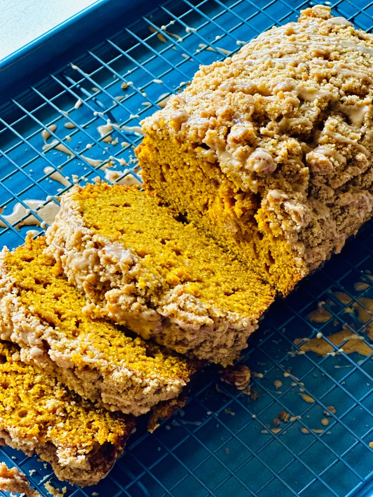A loaf of pumpkin spice crumb cake on a wire rack topped with pumpkin-spice glaze