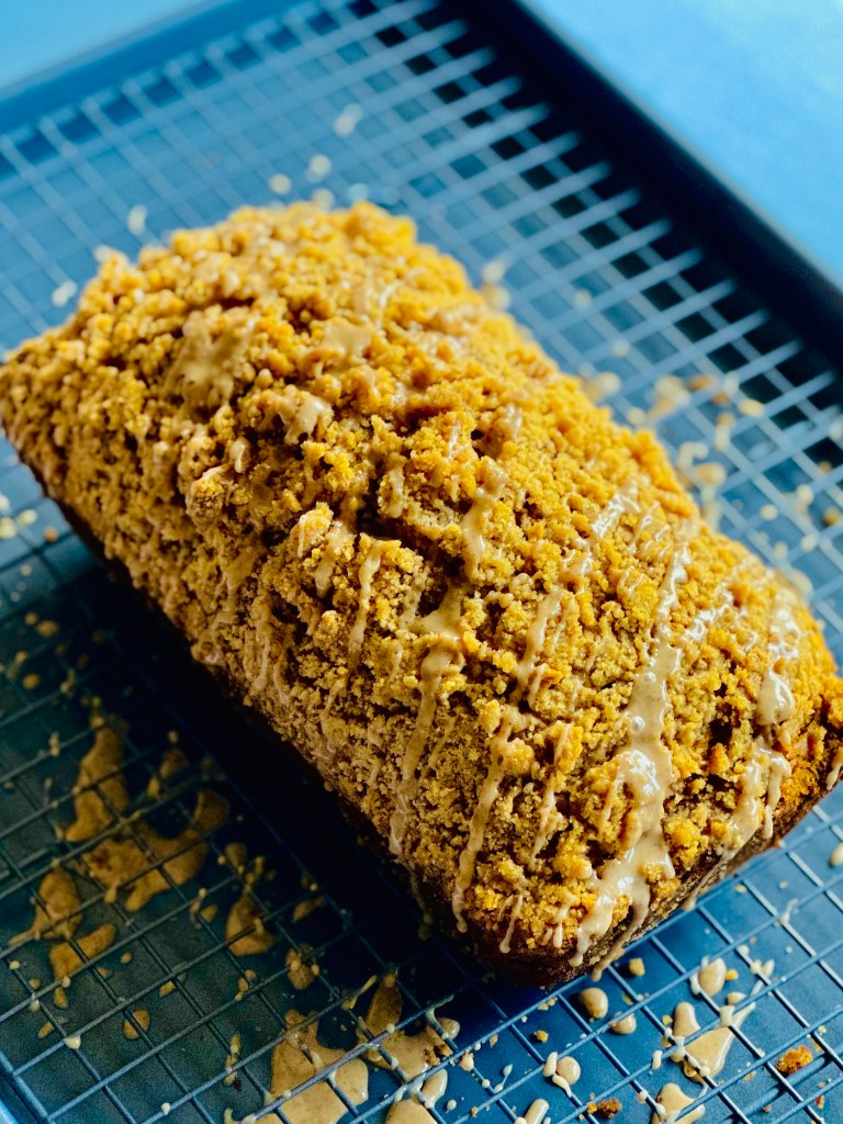 A loaf of pumpkin spice crumb cake on a wire rack topped with pumpkin-spice glaze