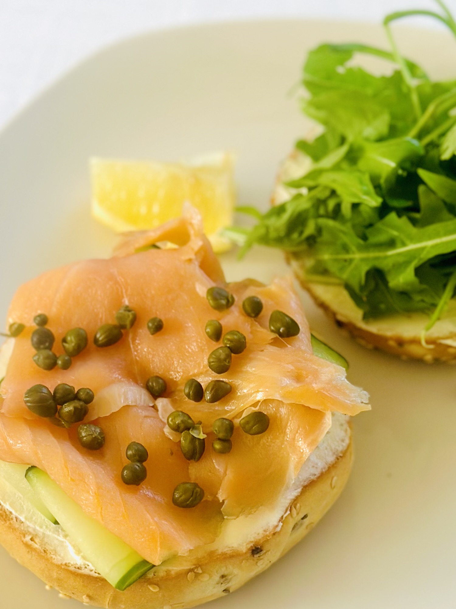 A bagel sandwich with cream cheese, cucumber, smoked salmon, capers, and arugula