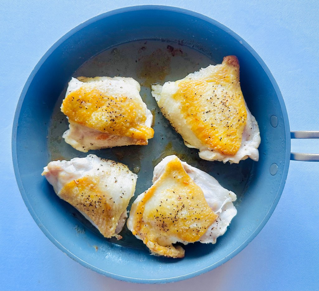 A skillet with bone-in, skin-on chicken thighs cooking in olive oil
