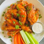 A plate of buffalo chicken wings garnished with chopped parsley and served with celery and carrot sticks