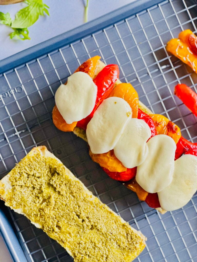 A sheet pan with roasted peppers and melted mozzarella on top of a slice of ciabatta bread