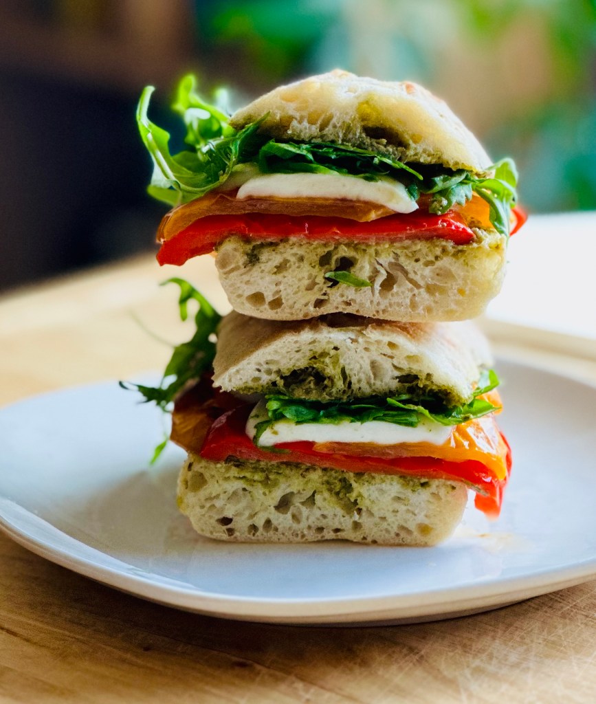 A photo of a roasted pepper, mozzarella, and pesto sandwich on a serving plate