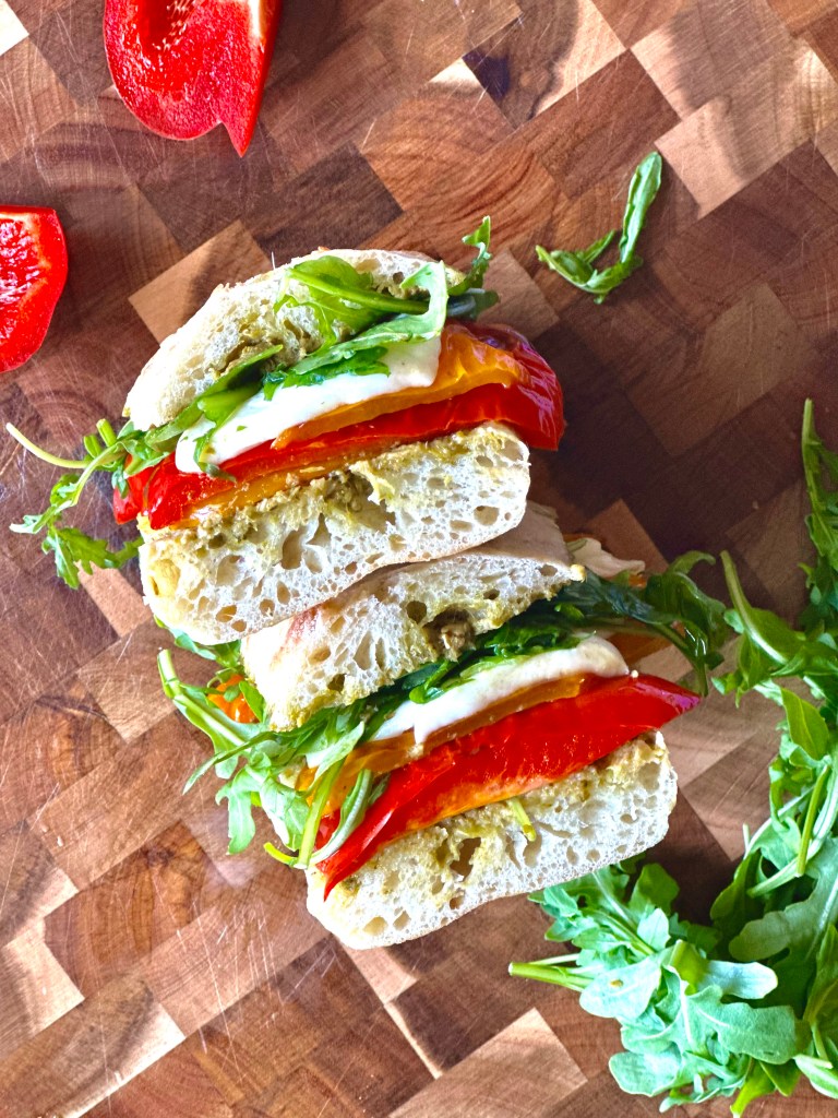 A photo of a roasted pepper, mozzarella, and pesto sandwich on a cutting board