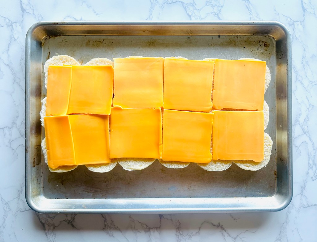 Slider buns being prepared with sliced cheddar cheese