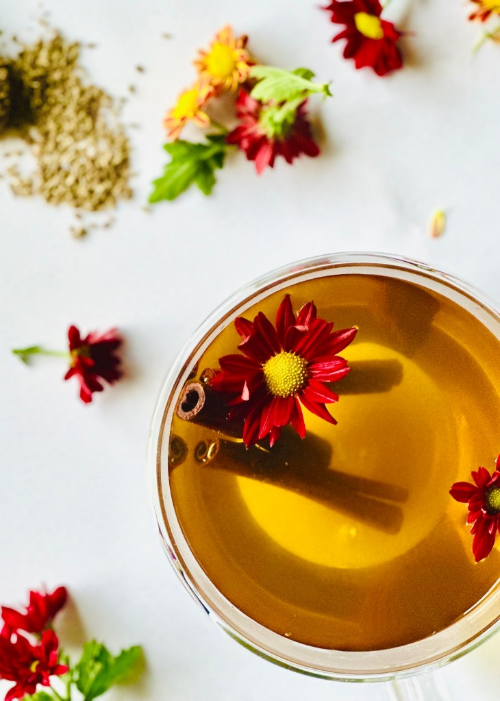 A clear mug full of freshly brewed anise seed tea with cinnamon sticks and edible flowers