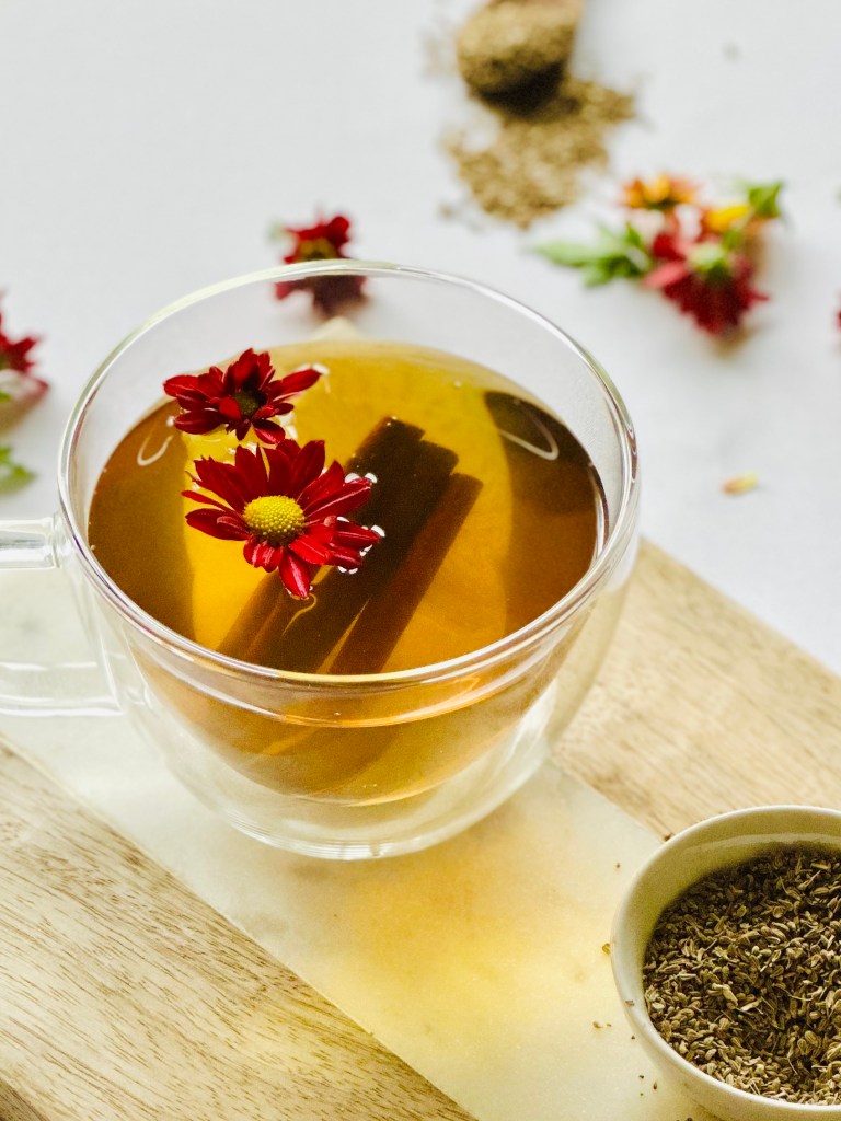 A clear mug full of freshly brewed anise seed tea with cinnamon sticks and edible flowers
