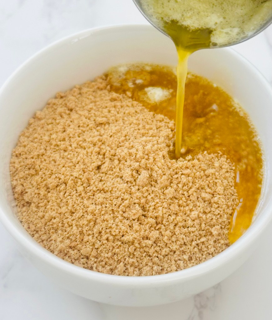 Graham cracker crumbs with melted butter being poured on top
