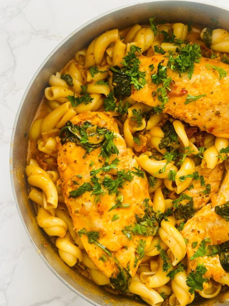 A large pan of Marry Me Chicken nestled with pasta and a garnish of parsley