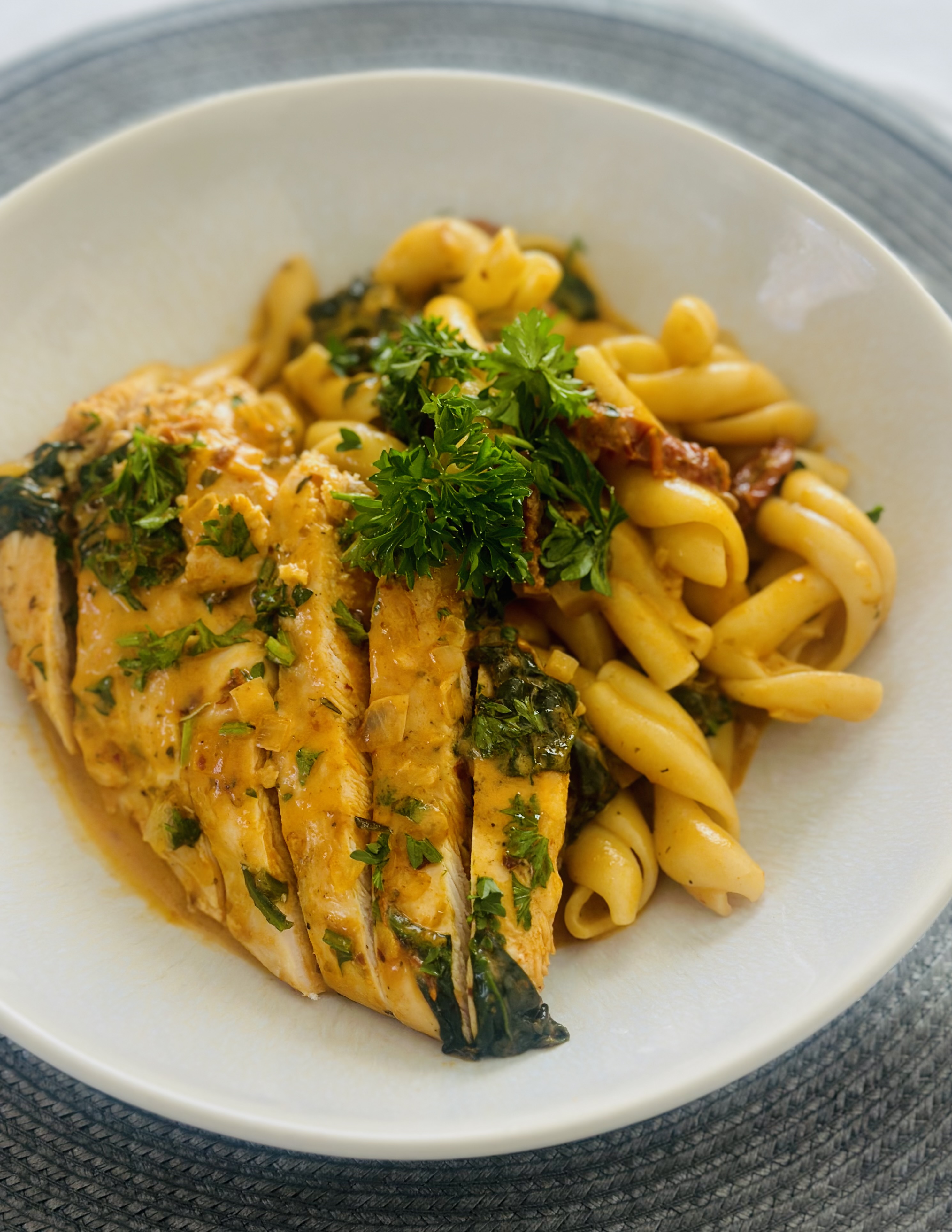 A serving plate of Marry Me Chicken served alongside pasta with a garnish of parsley