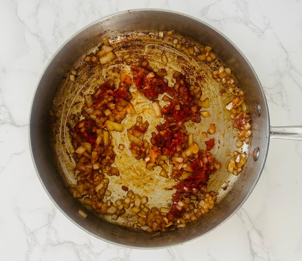 Chopped onion and garlic being sauteed with tomato paste
