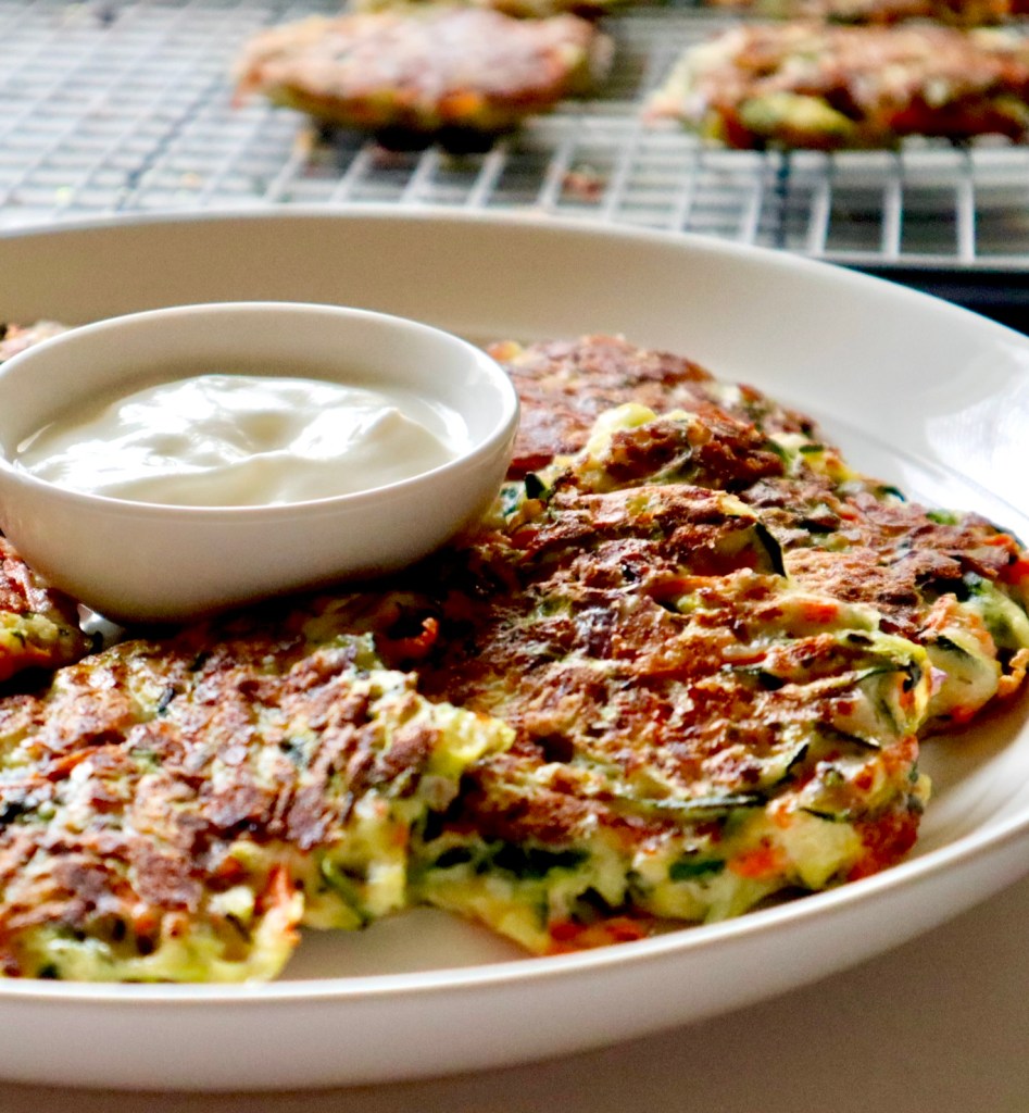 Crispy zucchini fritters on a plate with a serving of tzatziki