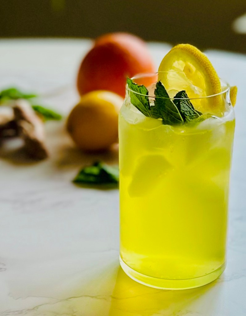 A glass of iced tea with citrus, ginger, and other cold relief ingredients, garnished with a sprig of fresh mint