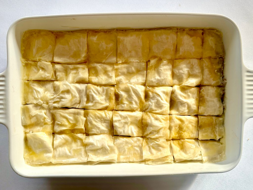 A photo of savory baklava being assembled with phyllo dough in a baking dish