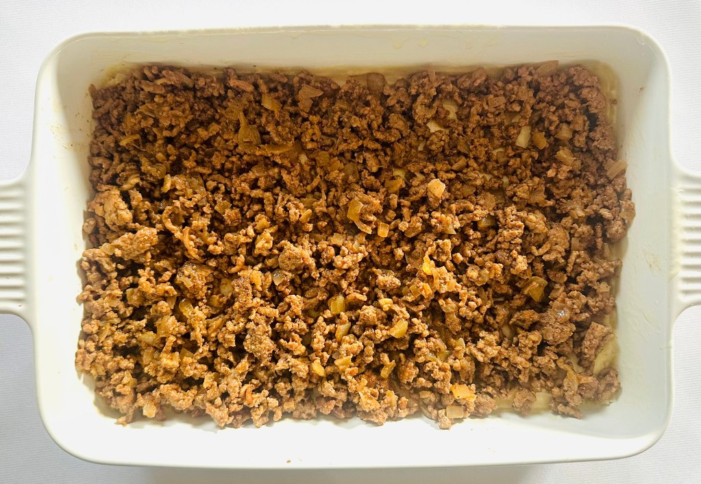 A layer of ground beef and onion in a baking dish