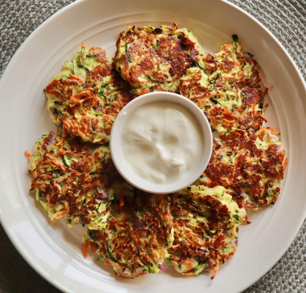 Crispy zucchini fritters on a plate with a serving of tzatziki