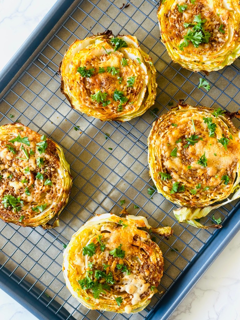 A baking sheet of oven-roasted cabbage steaks with melted Parmesan cheese and parsley for garnish
