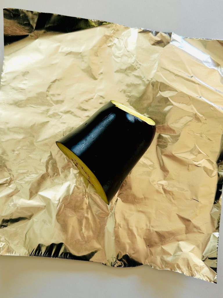 A photo of a halved eggplant being wrapped in aluminum foil
