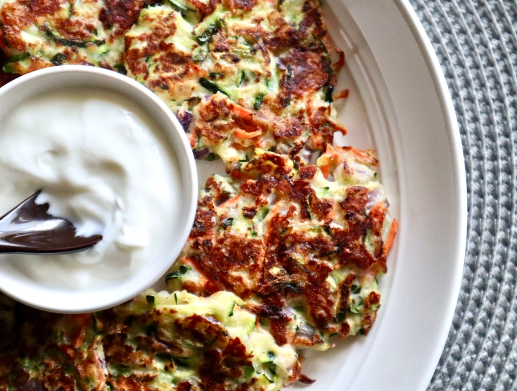 Crispy zucchini fritters on a plate with a serving of tzatziki