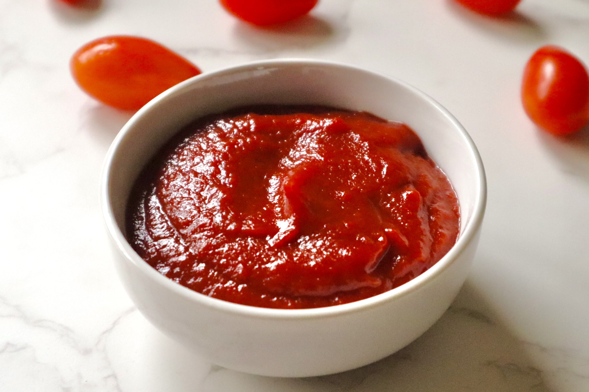 A bowl of homemade ketchup with cherry tomatoes in the background