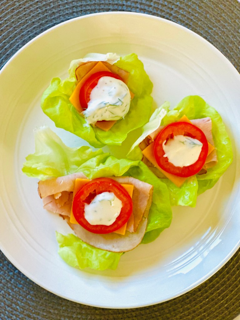 Lettuce wraps on a plate topped with turkey lunchmeat, cheddar cheese, roma tomatoes, and a dill-yogurt dressing