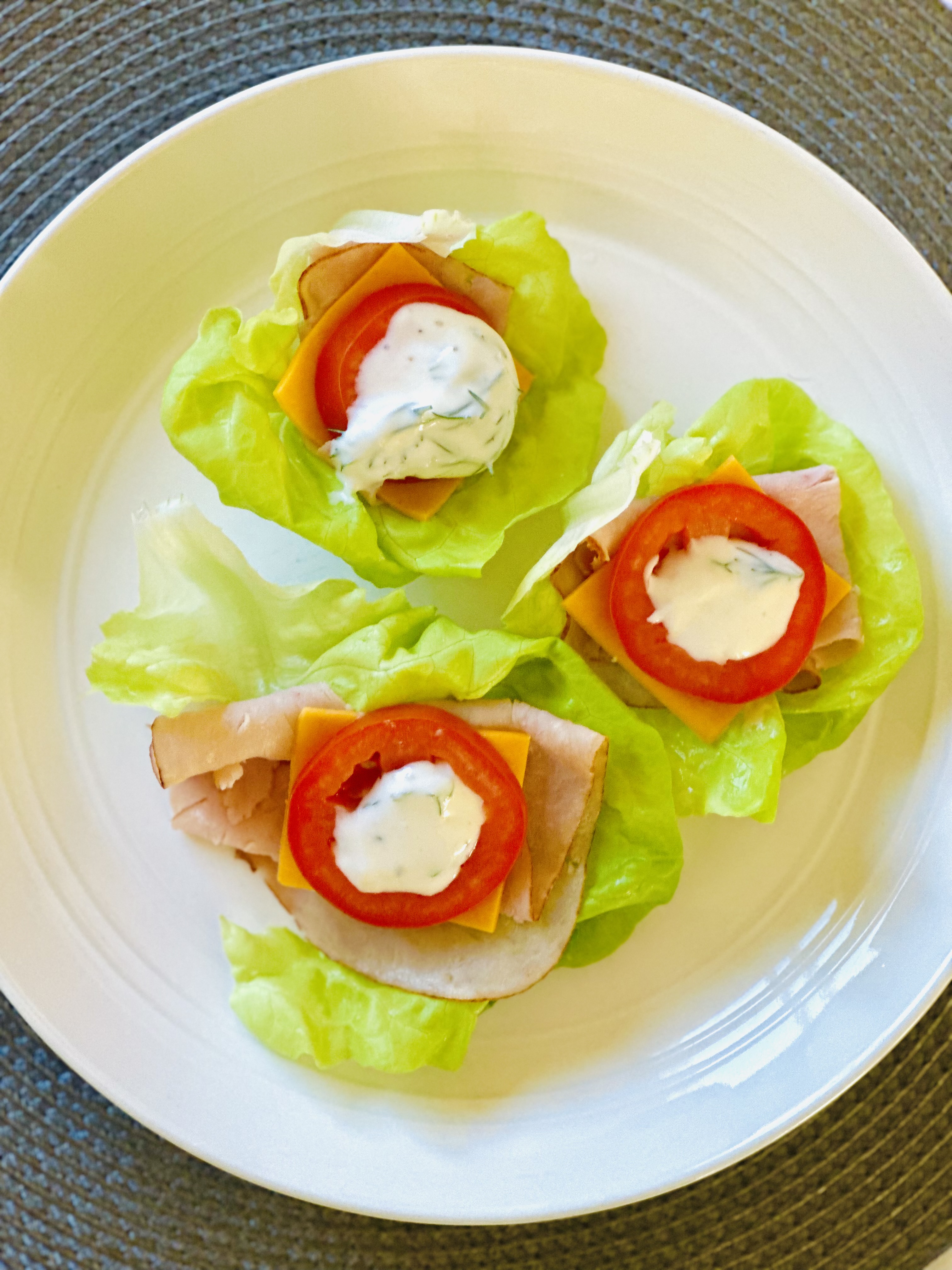 Lettuce wraps on a plate topped with turkey lunchmeat, cheddar cheese, roma tomatoes, and a dill-yogurt dressing