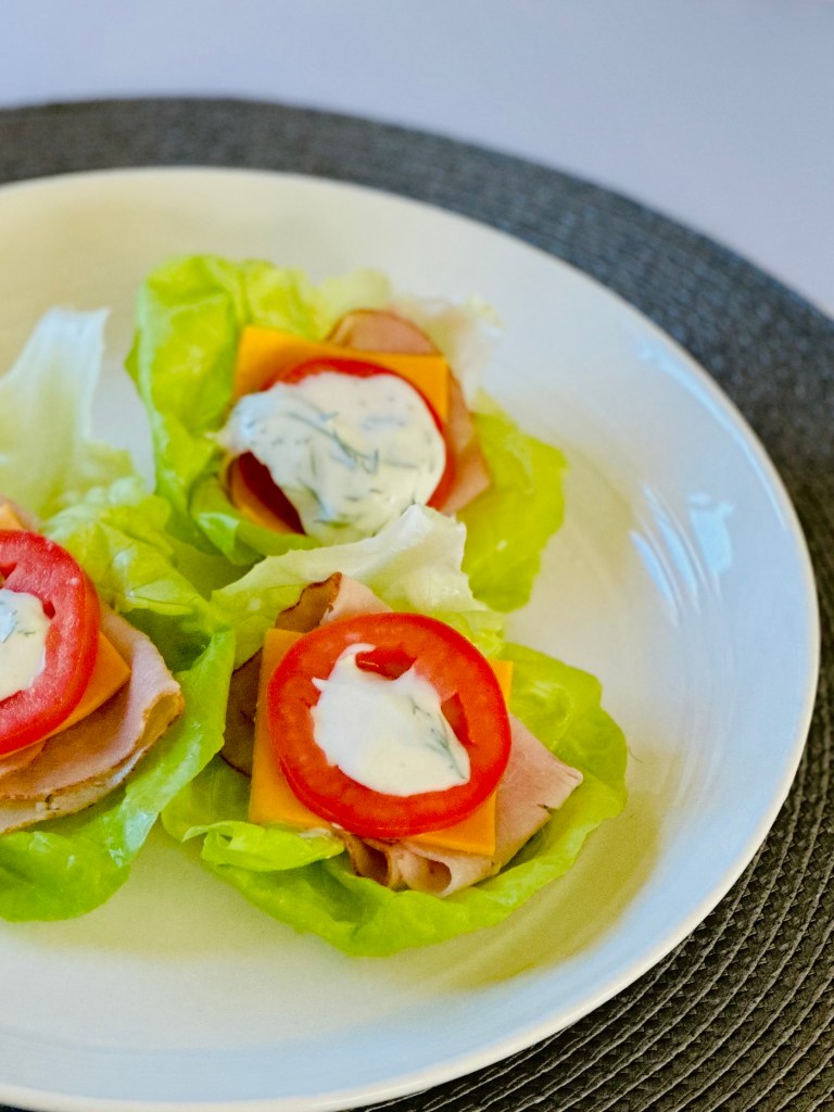Lettuce wraps on a plate topped with turkey lunchmeat, cheddar cheese, roma tomatoes, and a dill-yogurt dressing