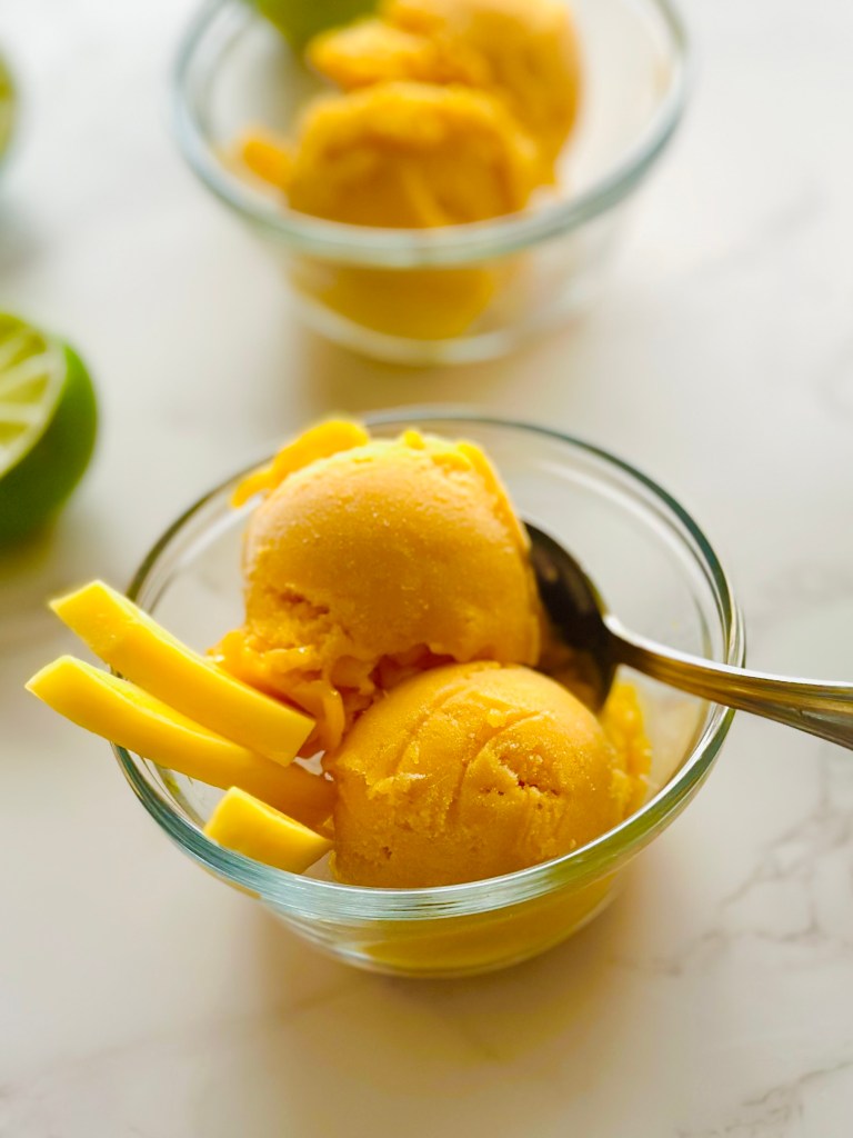 Two bowls of homemade mango sorbet garnished with fresh mango slices