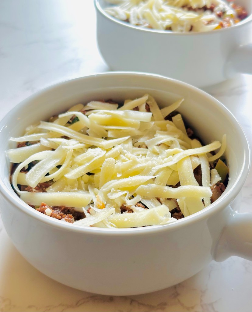 Bowl of cooked ground beef and marinara sauce topped with shredded mozzarella