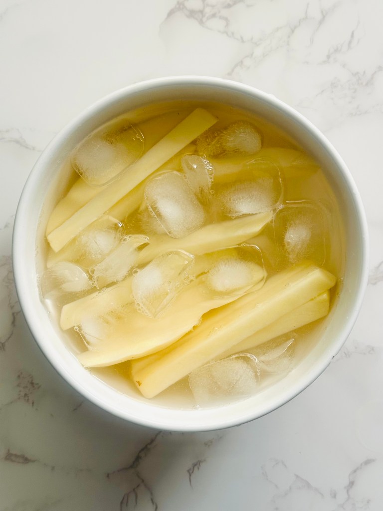 Sliced russet potatoes submerged in a bowl of ice water