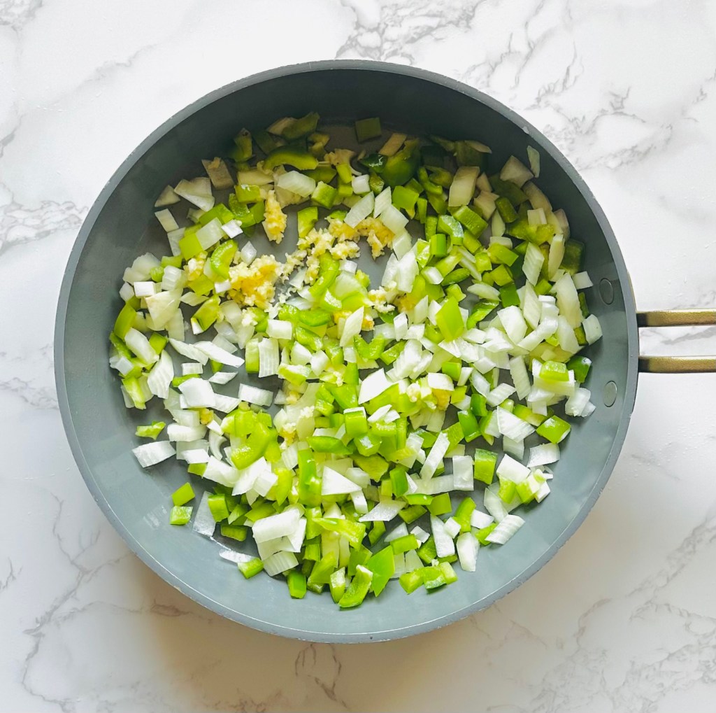 A photo of chopped onion, green bell pepper, and garlic being sautéed