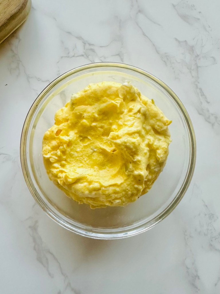 A glass bowl of deviled egg filling made with egg yolks, mayo, pickle relish, yellow mustard, and hot sauce