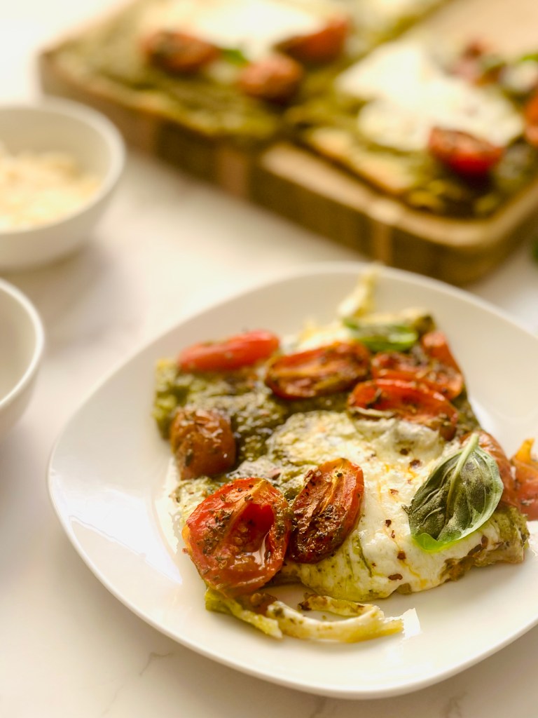 A slice of oven-baked sheet pan pizza with pesto, roasted tomatoes, and melted buffalo mozzarella cheese