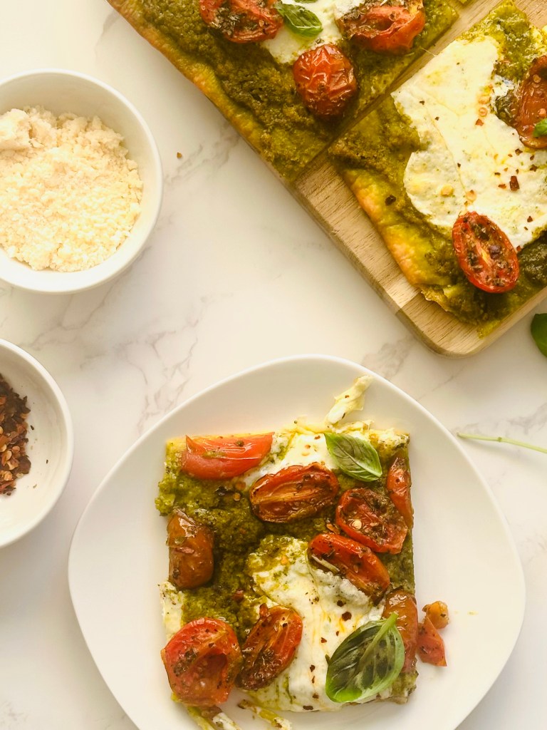 A slice of oven-baked sheet pan pizza with pesto, roasted tomatoes, and melted buffalo mozzarella cheese