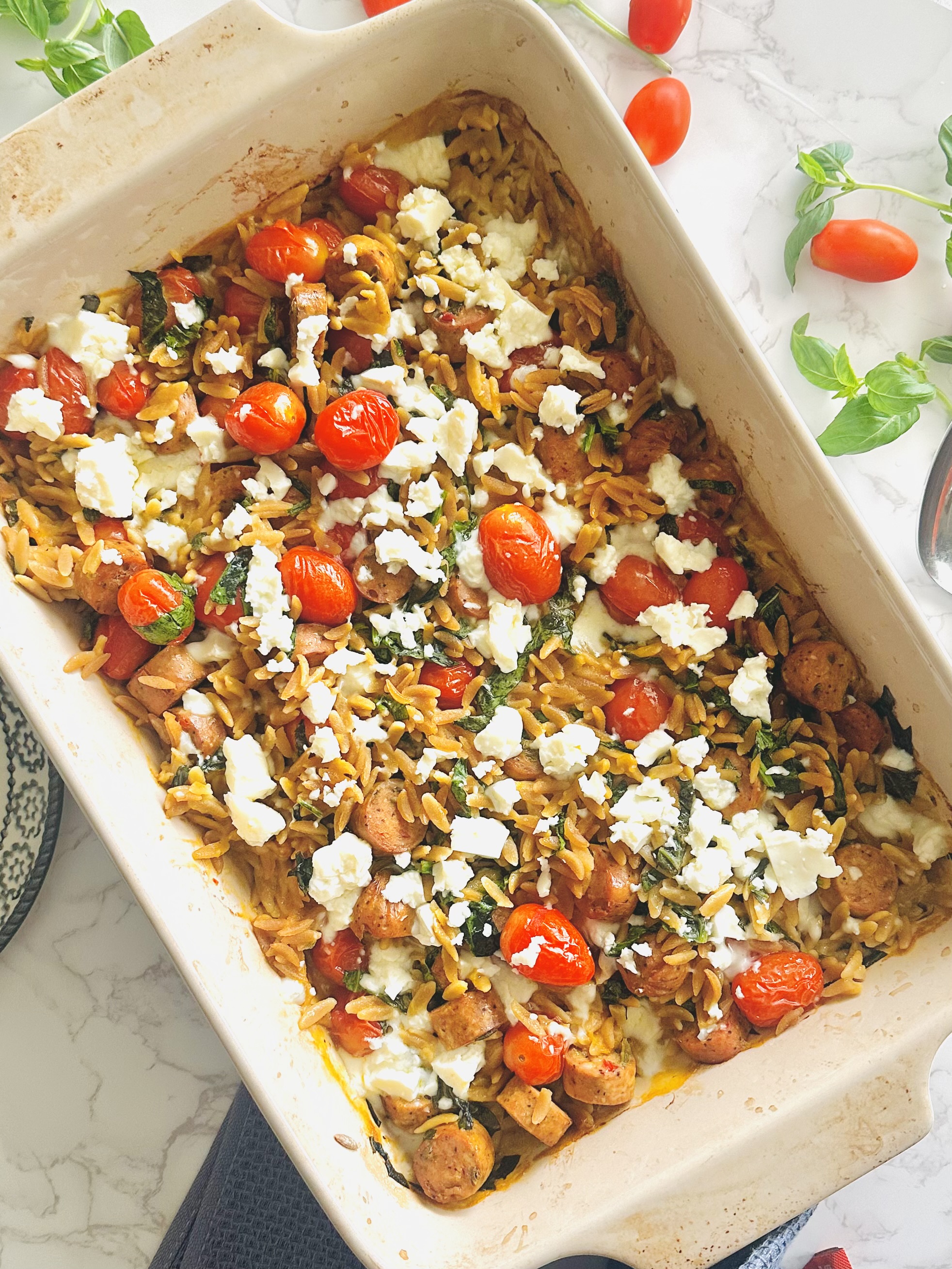 Homemade one-pan baked meal with feta, sausage, spinach, tomatoes, and orzo, fresh out of the oven
