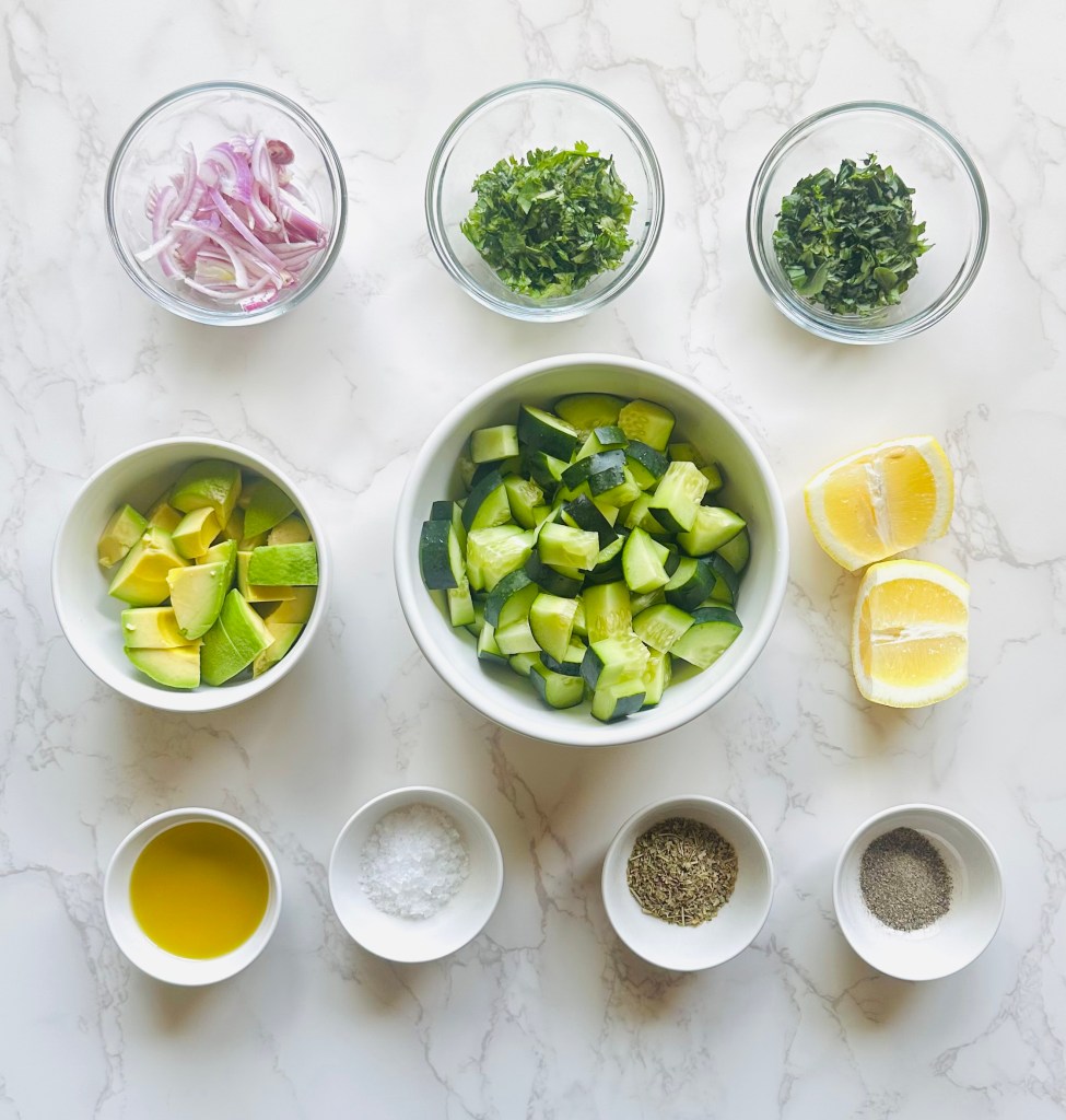 A photo of ingredients used to make a cucumber avocado salad with fresh herbs and red onion