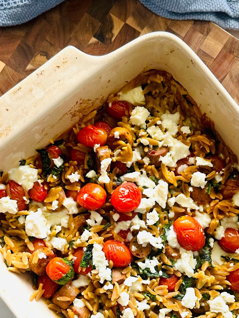 Homemade one-pan baked meal with feta, sausage, spinach, tomatoes, and orzo, fresh out of the oven