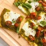 Oven-baked sheet pan pizza with pesto, roasted tomatoes, and melted buffalo mozzarella cheese