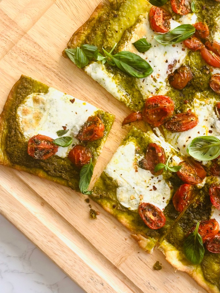 Oven-baked sheet pan pizza with pesto, roasted tomatoes, and melted buffalo mozzarella cheese