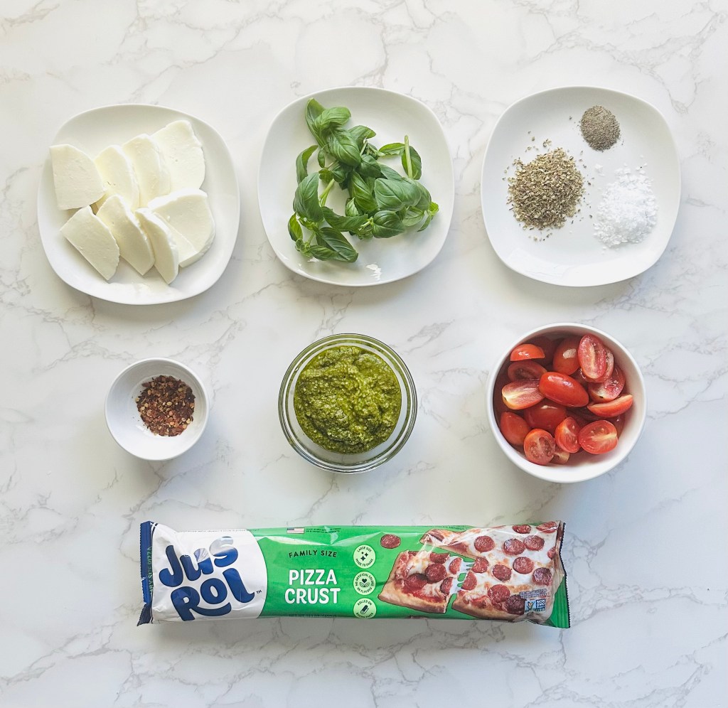 A photo of ingredients used to make sheet pan pizza with store-bought dough, tomatoes, basil, and mozzarella