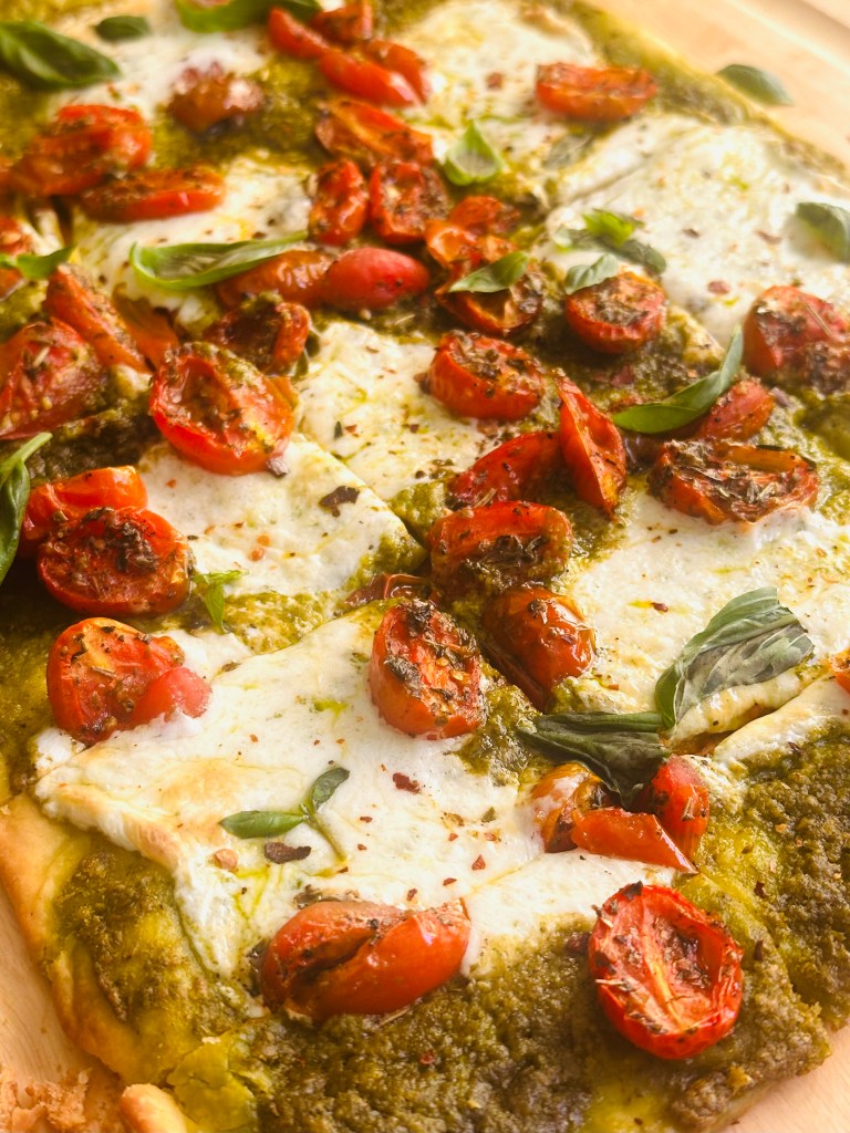 Oven-baked sheet pan pizza with pesto, roasted tomatoes, and melted buffalo mozzarella cheese