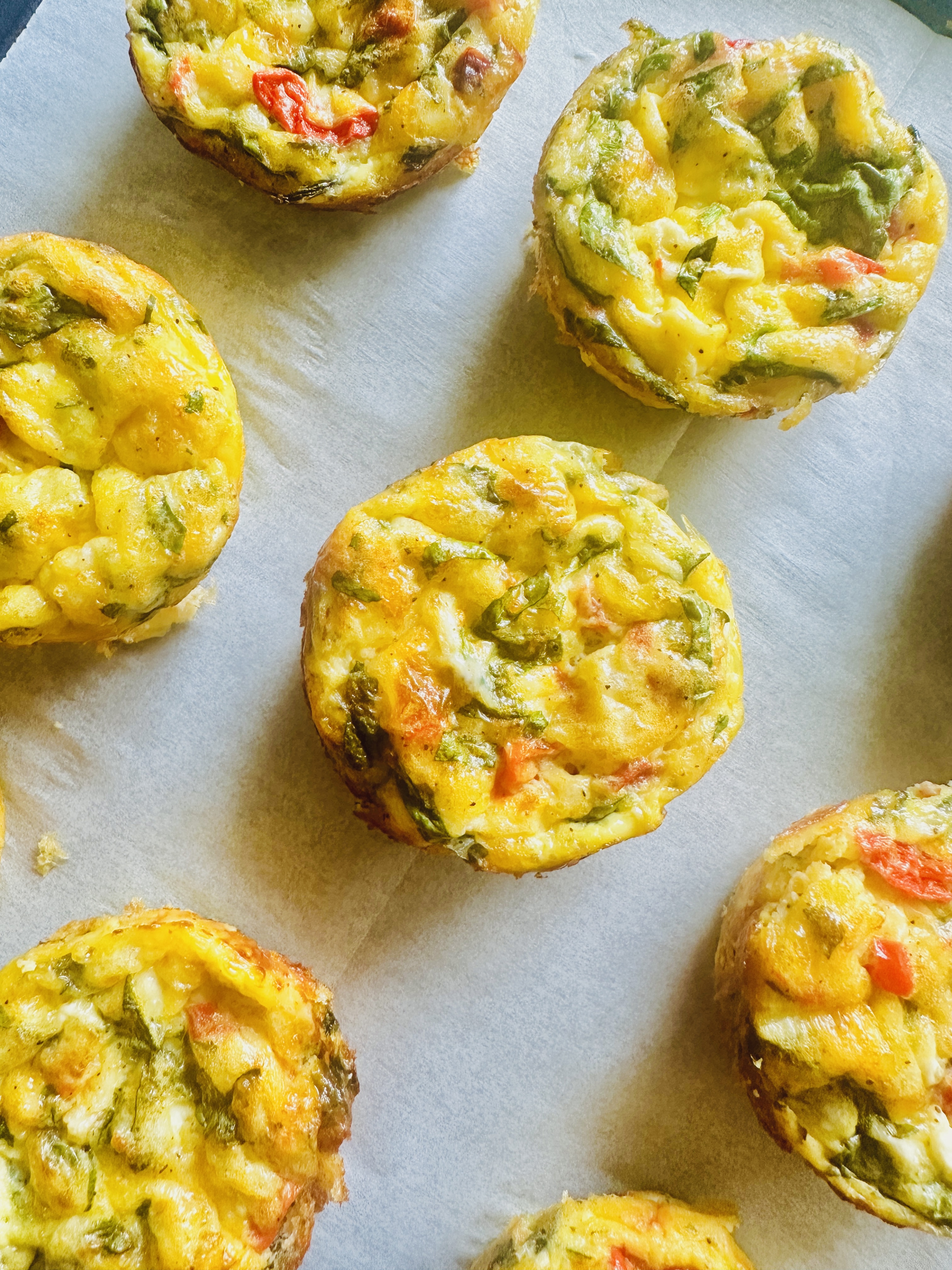 A row of cottage cheese egg bites filled with eggs, cottage cheese, spinach, roasted red pepper, and shredded Mexican cheese
