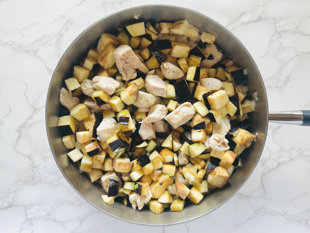 Chicken breast, eggplant, and diced onion being sautéed in a skillet