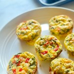 A white platter of cottage cheese egg bites, made with eggs, cottage cheese, spinach, roasted pepper, and shredded Mexican cheese
